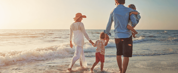 family walking down beach while carrying toddler.